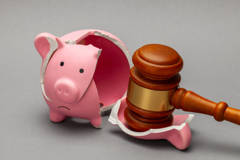 A pink piggy bank broken by a judges gavel on a grey surface