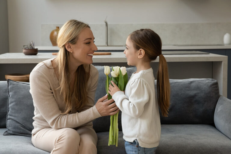 Mother on grey couch holding tulips with her daughter and both are smiling