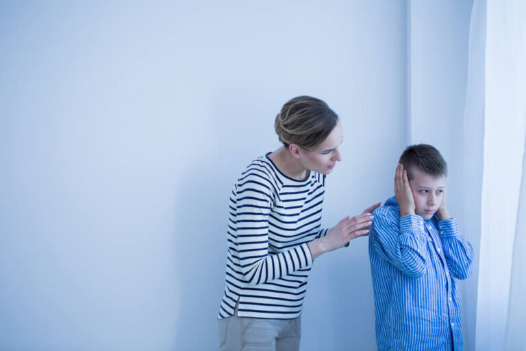 Mother behind her son talking to him and the boy has his ear covered with his hands