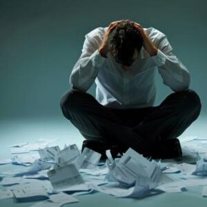 Man with head down and hands on his head, stressing over papers all over the floor worry about business bankruptcy or personal bankruptcy