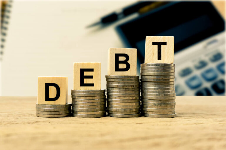 Wooden blocks spelling out the word debt on a stack of coins the increases as the word is spelled