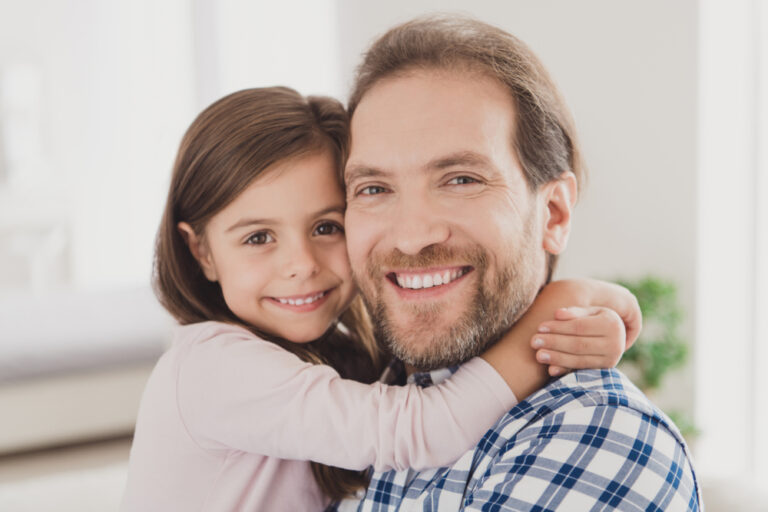 A man and a little girl, possibly her father, hugging affectionately in the living room.