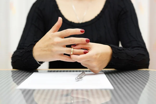 In a quiet moment at a Dallas, TX café, a person with red nail polish carefully removes a ring from their finger. Nearby, next to the reflective table surface, lie key factors—a pen and paper—perhaps notes for their meeting with a divorce attorney.