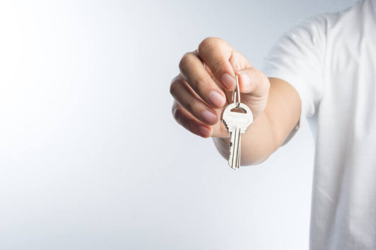 A man standing in front of a white background and he is holding his are out with keys in his hand