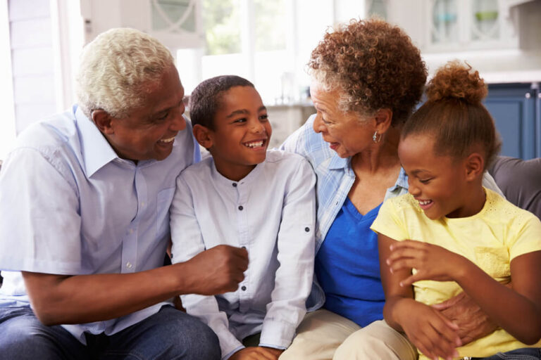 Two grandparents sitting on the couch with their grandson and granddaughter and they are all laughing