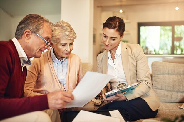 An older couple reviews  documents with a professional woman on a couch in a cozy living room setting.