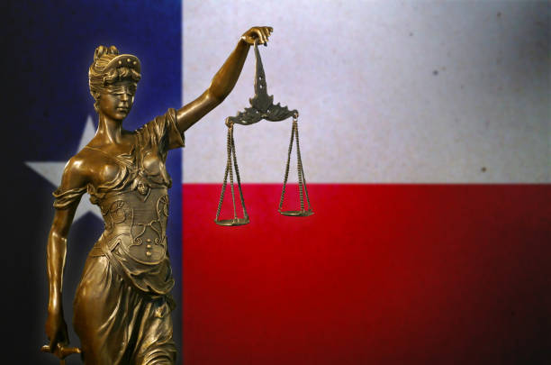 Close-up of a small bronze statuette of Lady Justice before a flag of Texas.