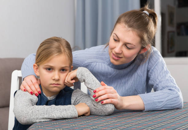 An adult woman, who may be wondering if a mother can cancel child support in Texas, comforts a young girl who appears upset, sitting at a table indoors.