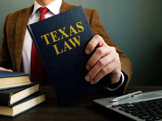 A bankruptcy attorney in Garland, TX holds a book titled "Texas Law" near a laptop and a pen on the desk.