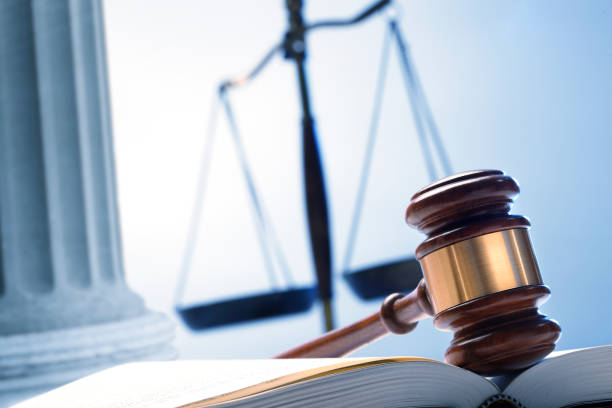 A gavel rests on top of an open law book with a justice scale and a Greek column in the background.