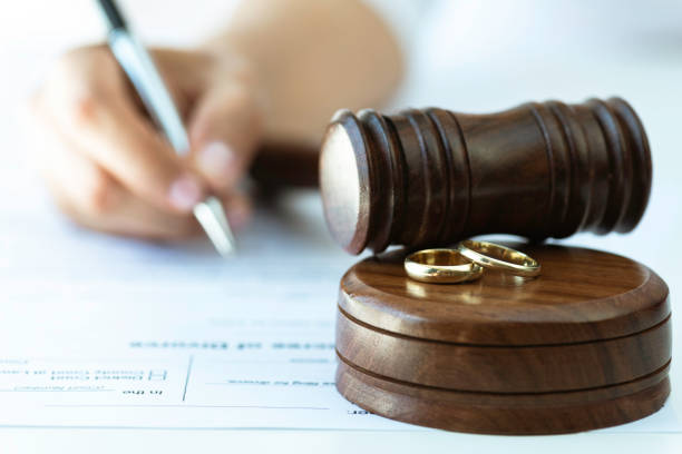 Weeding rings and gavel with a person signing a contract in the background. Representing justice steps of divorce process.