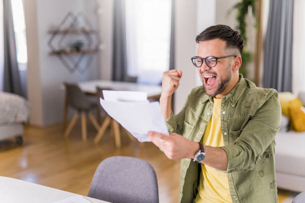 Shot of a young man celebrating while going over paperwork at home.