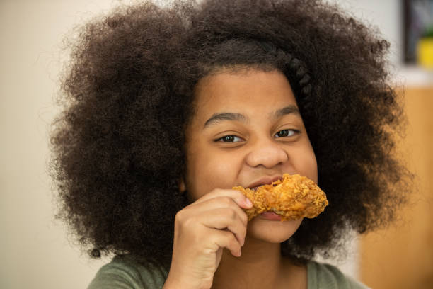 Close up of Little African girl biting delicious deep fried chicken with happiness. Happy family enjoy having dinner with eating and sharing a meal together at home., school meat recall