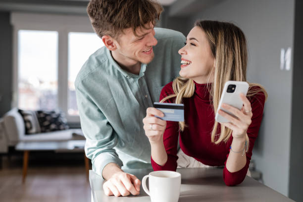 Happy couple smiling and looking at each other while shopping online via smartphone