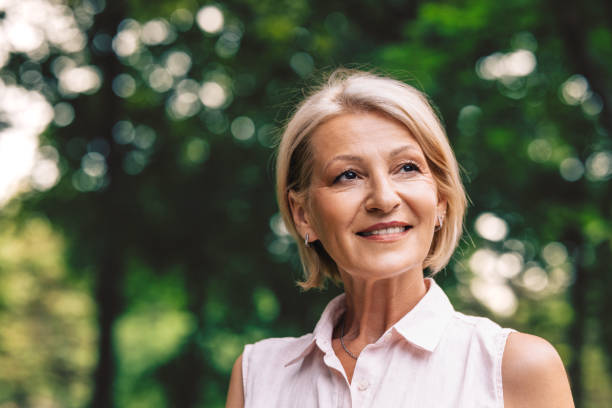 A portrait of a smiling senior Caucasian female contemplating while standing outdoors.