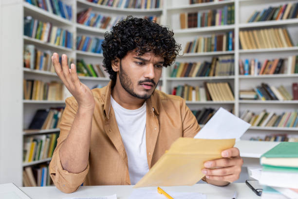 Young hispanic student upset studying inside university campus academic library, disappointed and sad received a letter with bad results in studies and entrance exam.