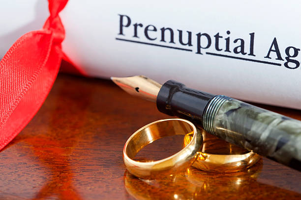 A rolled-up prenuptial agreement tied with a red ribbon lies next to two gold wedding bands and a fountain pen on a wooden surface, prompting the question: are prenups valid in Texas?