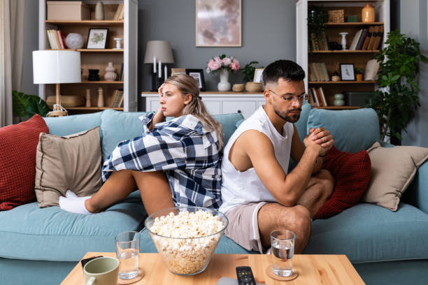 Stressed young married couple sitting separately on different sides of sofa ignoring each other after quarrel. Offended spouses not talk communicate feeling depressed disappointed after argue.