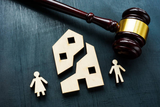 A judge's gavel is next to cut-out wooden figures of a man, a woman, and a split house, symbolizing divorce or separation.