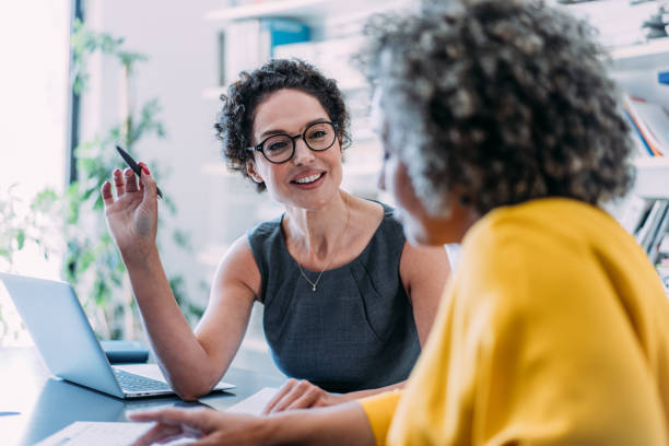 Shot of two beautiful businesswomen sharing ideas during a meeting in the office. Businesswomen discussing important documentation in the workplace. Two business people in office working on business reports.