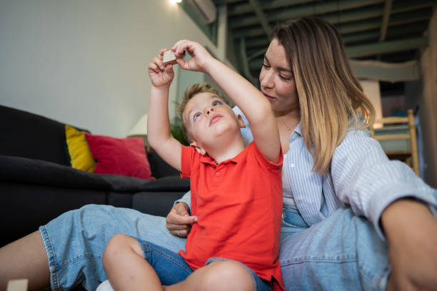 Young boy raising his arms while holding a wooden block with his mother watching him