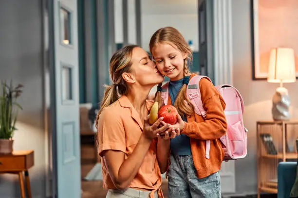 mother kissing her daughter before she leaves for school