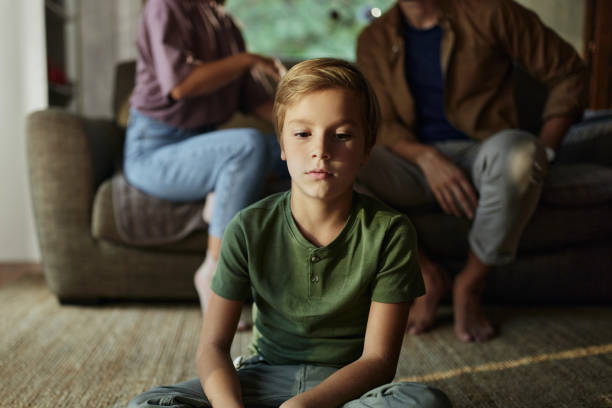 Sad little boy sitting in front of his parents who are arguing at home.