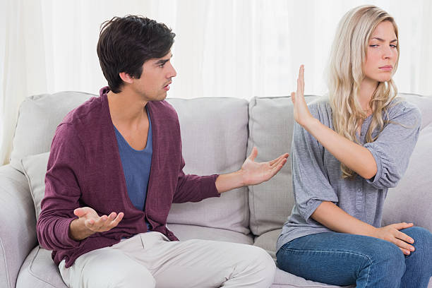 Furious blonde not listening to her pleading boyfriend at home on the sofa, divorce petty arguments