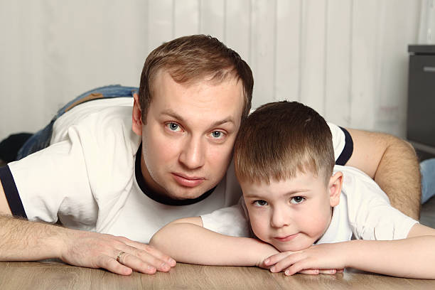 A man and a boy lying on the floor, resting their heads on their hands, gazing directly at the camera. Their close bond prompts one to wonder about family dynamics and questions like, "Can mother cancel child support in Texas?