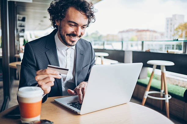 Smiling man sitting in cafe, holding a credit card and typing on a laptop, with copy space. credit card debt lawyer rockwall county texas