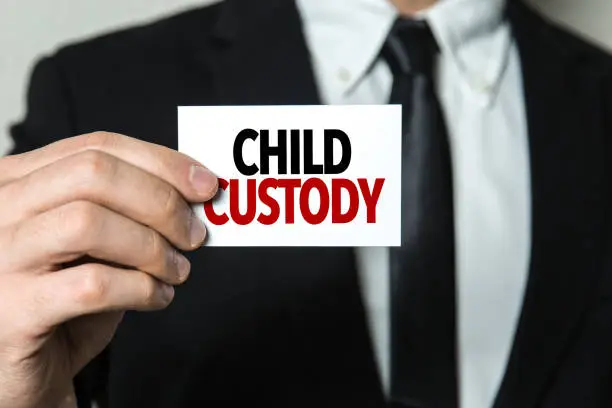 A person in a suit holds a card with the words "Child Custody" printed on it, symbolizing the expertise of a Garland Texas child custody lawyer.