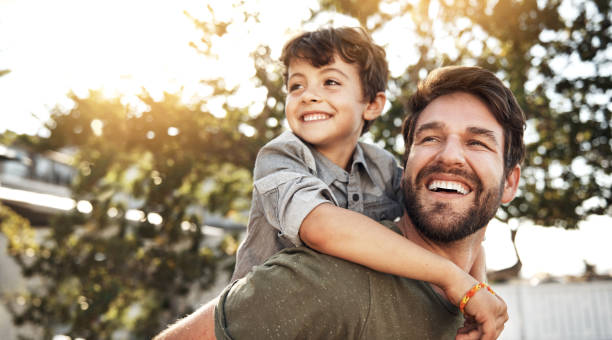 Portrait of a happy father giving his little boy a piggyback ride in their backyard