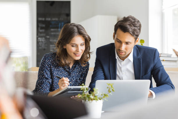 Two business people sitting at cafe working on new project using laptop. Young businesswoman taking notes and businessman working on laptop computer.