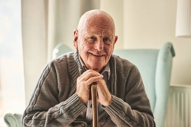 Portrait of happy senior man sitting at home with walking stock and smiling