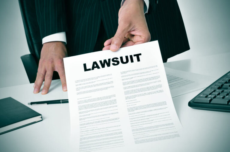 A man standing behind a desk holding up a paper that says lawsuit