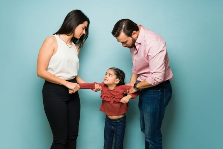 A little girl standing between her parents and each parent is pulling the girl a different direction