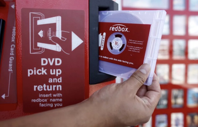 a man holding a red box dvd rental in his hand