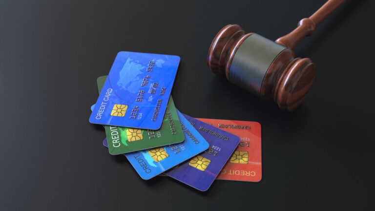 Five credit cards laid out on a black surface next to a judges gavel