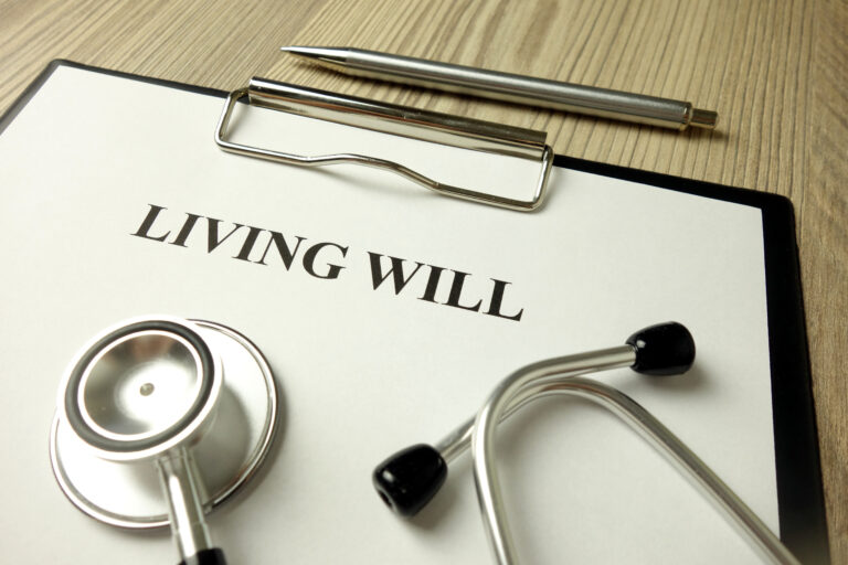 A clipboard with a document titled "Living Will", a stethoscope, and a pen on a wooden surface.