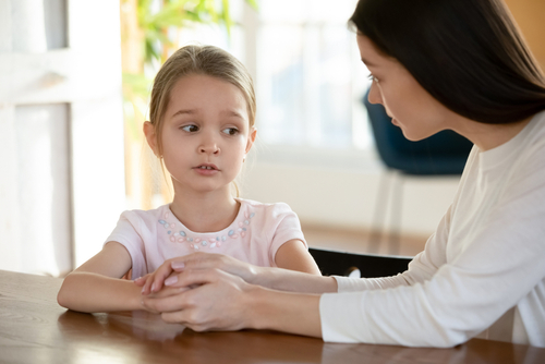A woman holding a young girl's hands at a table, both looking slightly to the side, suggesting a thoughtful conversation about important topics, perhaps even touching on questions like when child support ends in Texas.