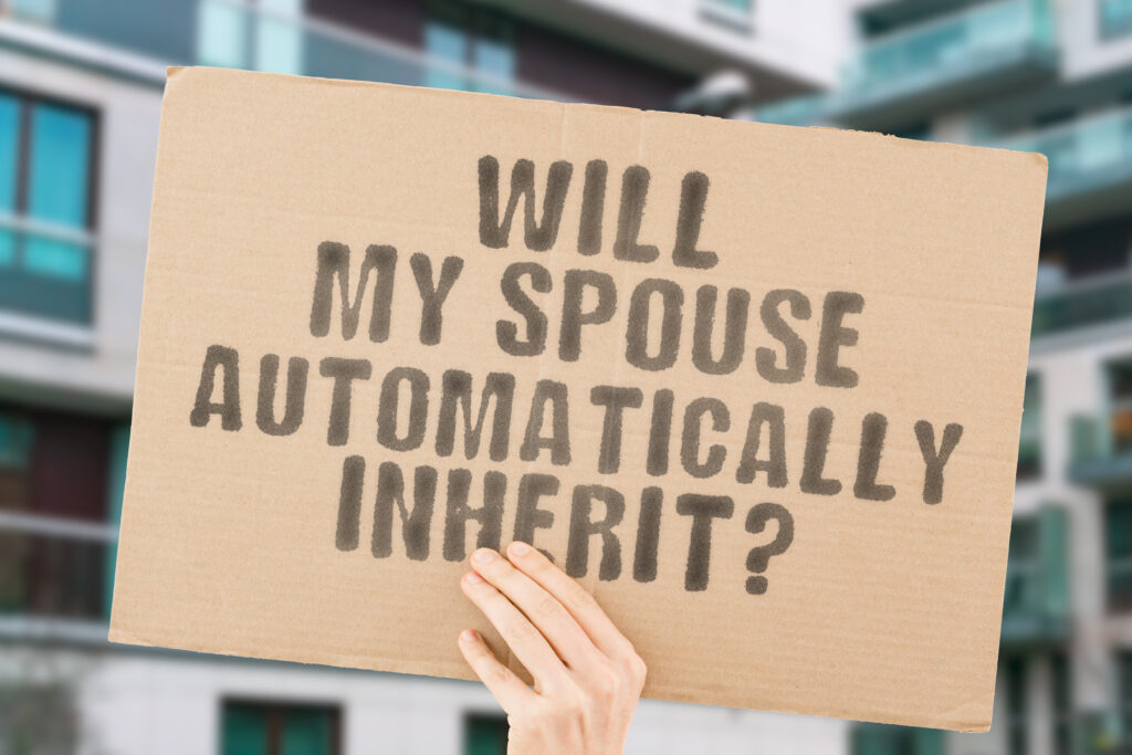 A hand holds a cardboard sign with the message "WILL MY SPOUSE AUTOMATICALLY INHERIT?" written in black letters in front of a blurred building background.