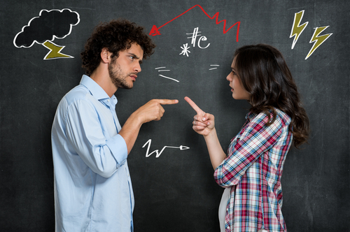 A man and woman stand facing each other, pointing fingers in disagreement, with doodles like lightning bolts and symbols on a chalkboard behind them