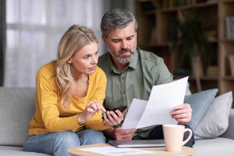 A man and woman sitting on the couch looking at papers and and the woman is holding a calculator