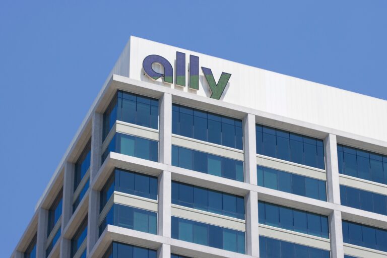 A building with a modern glass facade, featuring the "ally" logo in large letters on the top corner under a clear blue sky.