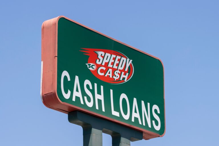 A green and red signboard against a clear blue sky, displaying the text "SPEEDY C$SH CASH LOANS.