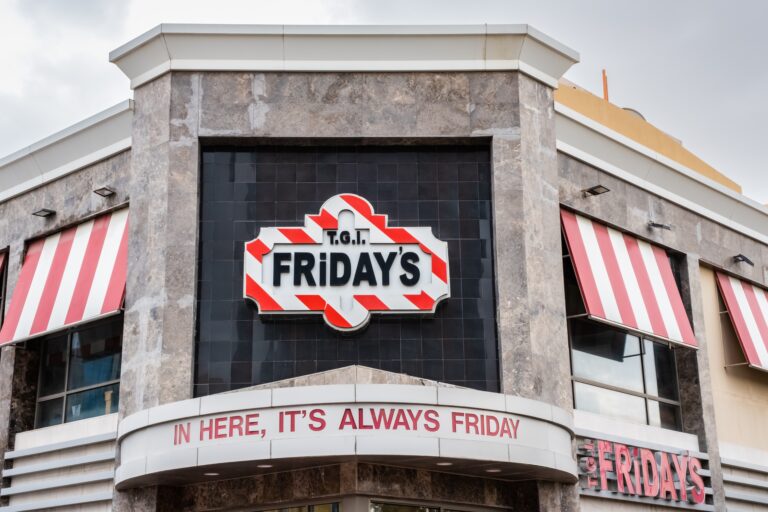 Restaurant exterior with a "T.G.I. Friday's" logo and striped red and white awnings. A sign reads, "In here, it's always Friday.