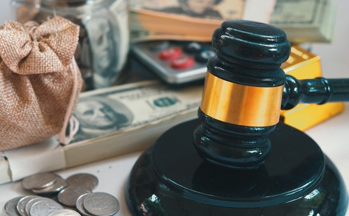 A judge's gavel surrounded by dollar bills, coins, a burlap sack, a calculator, and a gold bar paints a picture of finance and legal matters. This scene subtly hints at questions like who pays attorney fees in divorce cases in Texas.