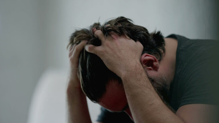 A close up of a man with his hands on his head in a dark room representing mental illness