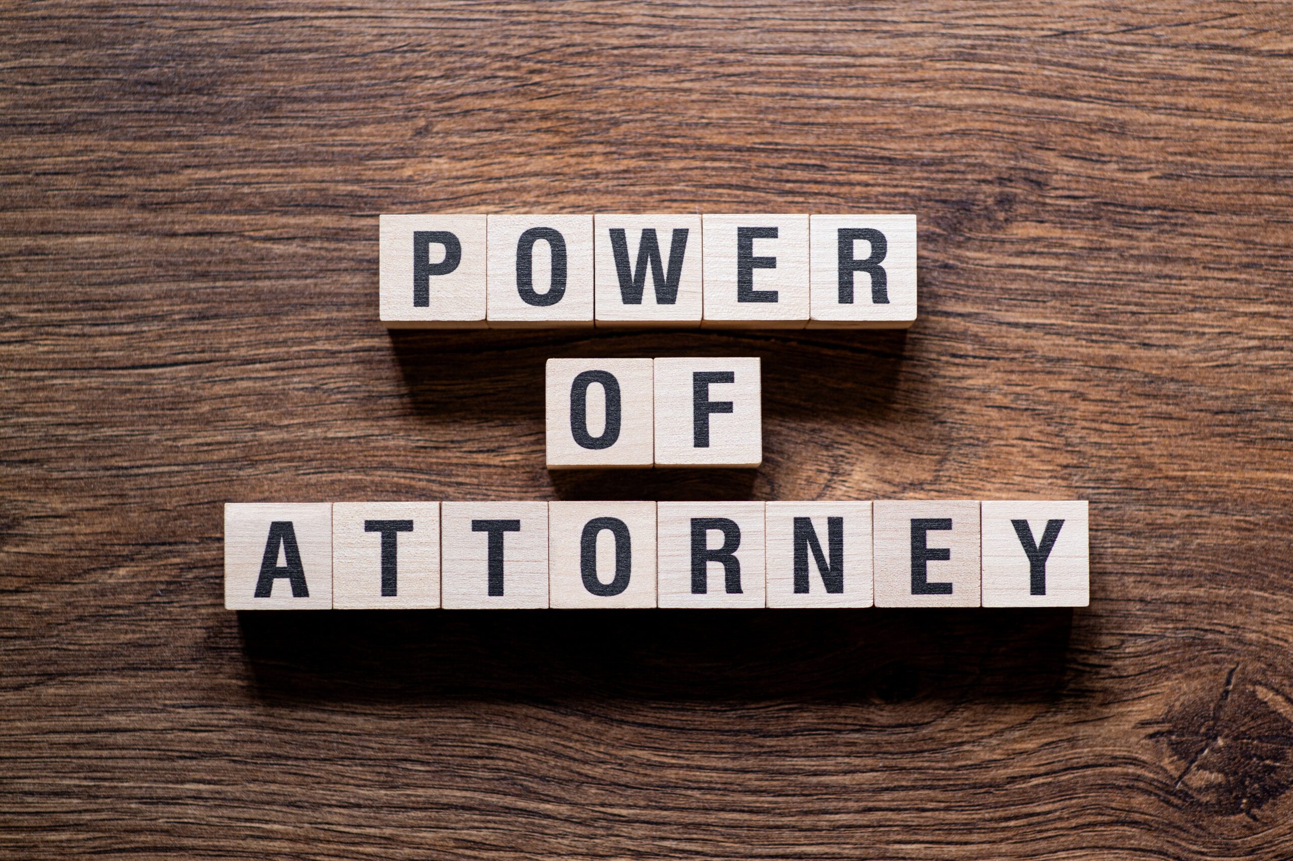 Wooden blocks arranged on a brown wooden surface spell out "Power of Attorney.