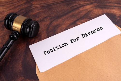 A judge's gavel rests on a wooden table beside an envelope marked "Petition for Divorce," hinting at the process of securing divorce papers in Texas.